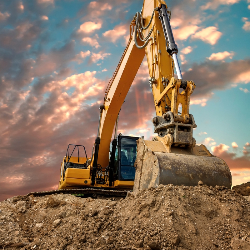 A large yellow excavator sits on a pile of dirt at a demolition site. This demolition in Alfords Point involves tearing down buildings and structures to make way for new construction or development.