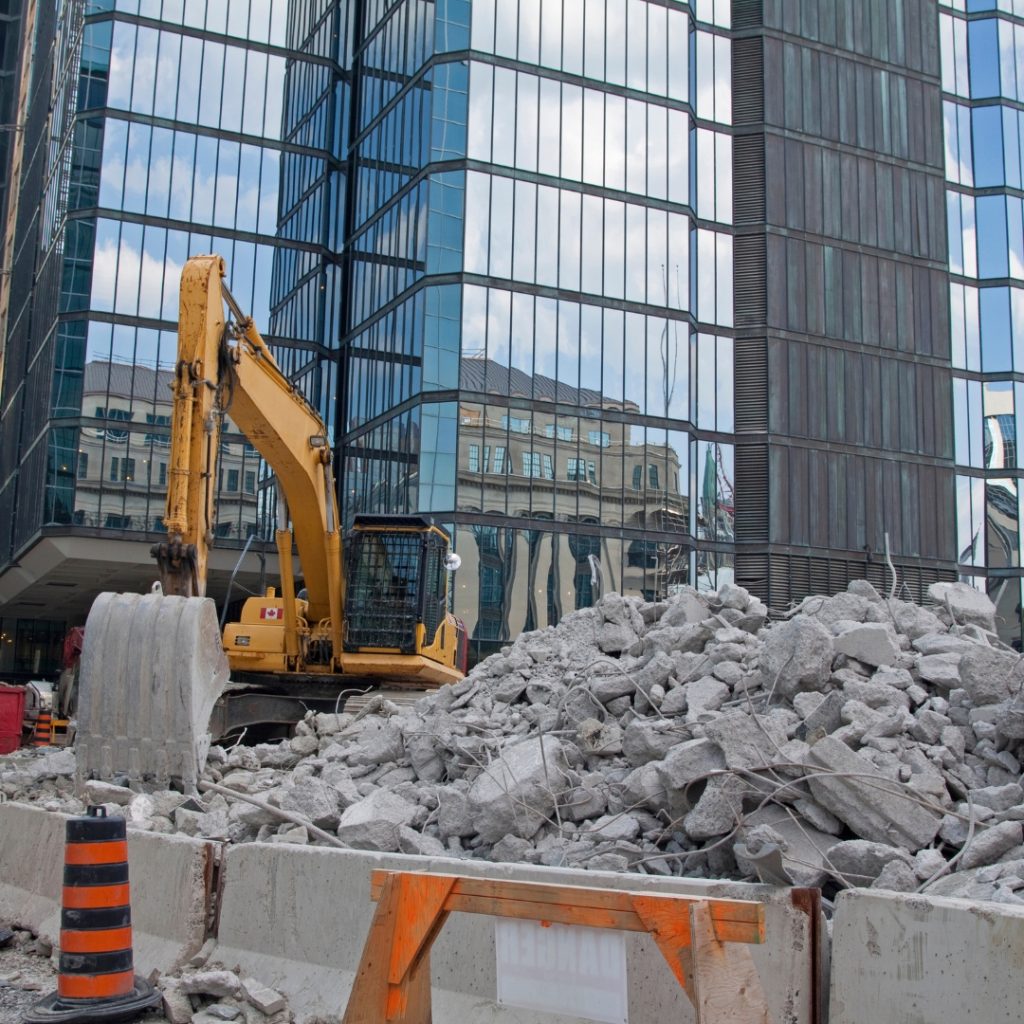 A construction site with a large pile of concrete debris in front of a tall building. This is a typical scene created by demolition contractors in Wombarra.